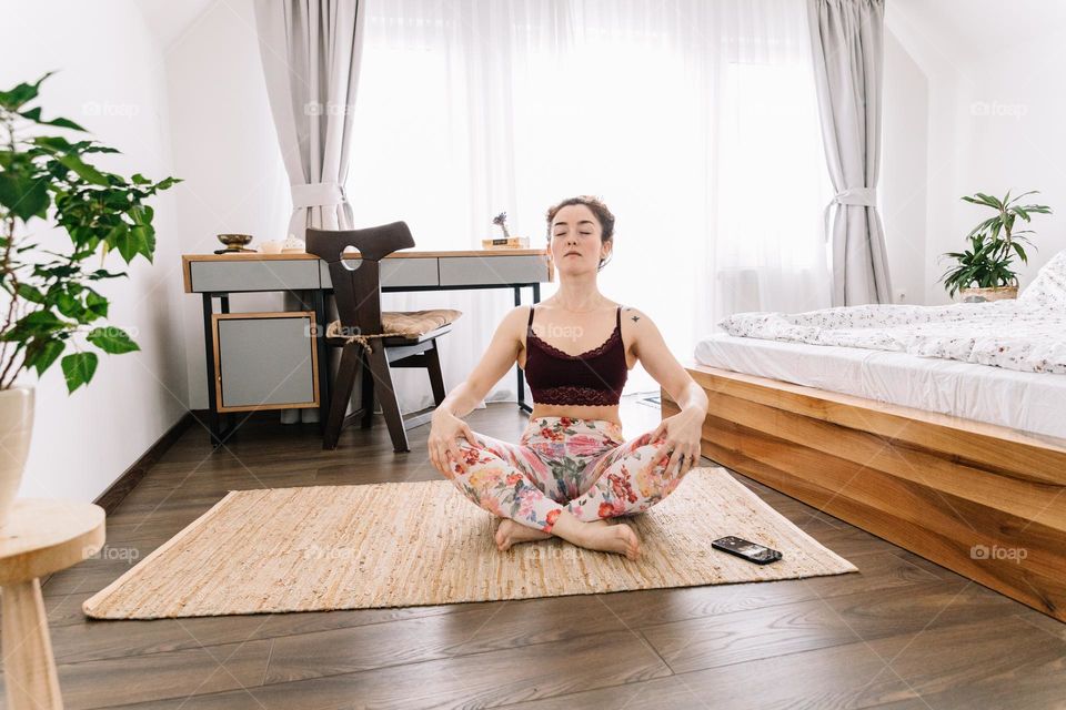 Millennial woman doing a yoga session at home, while dressed with colorful yoga pants and following instructions on her phone.