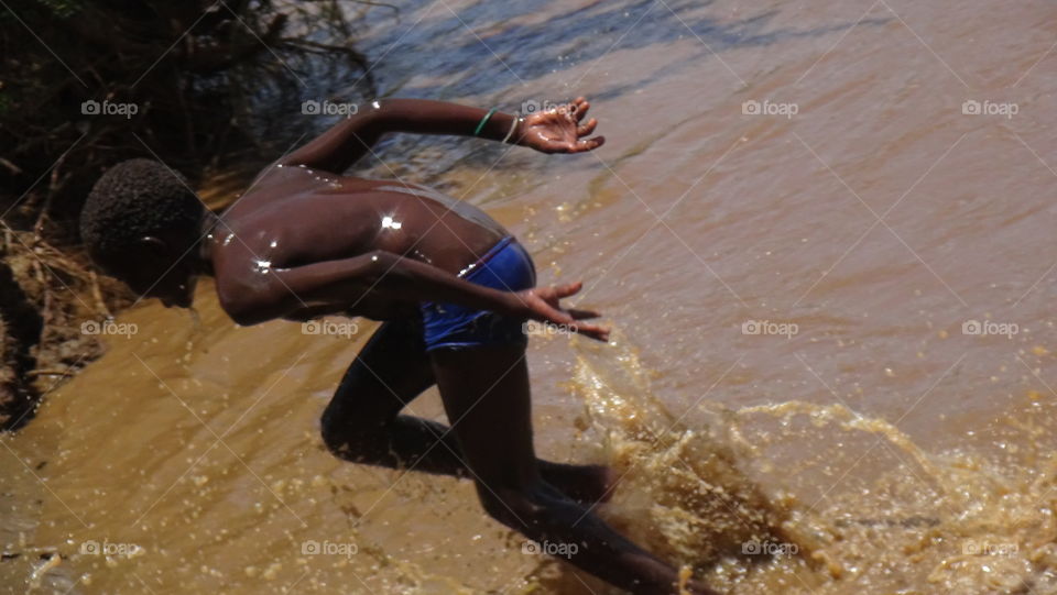A boy emerging from under the water from a river.