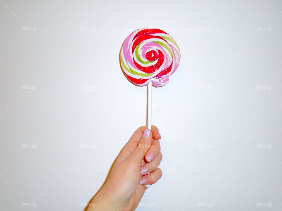 Hand of a woman with pink nail polish holding a lollipop on white background 