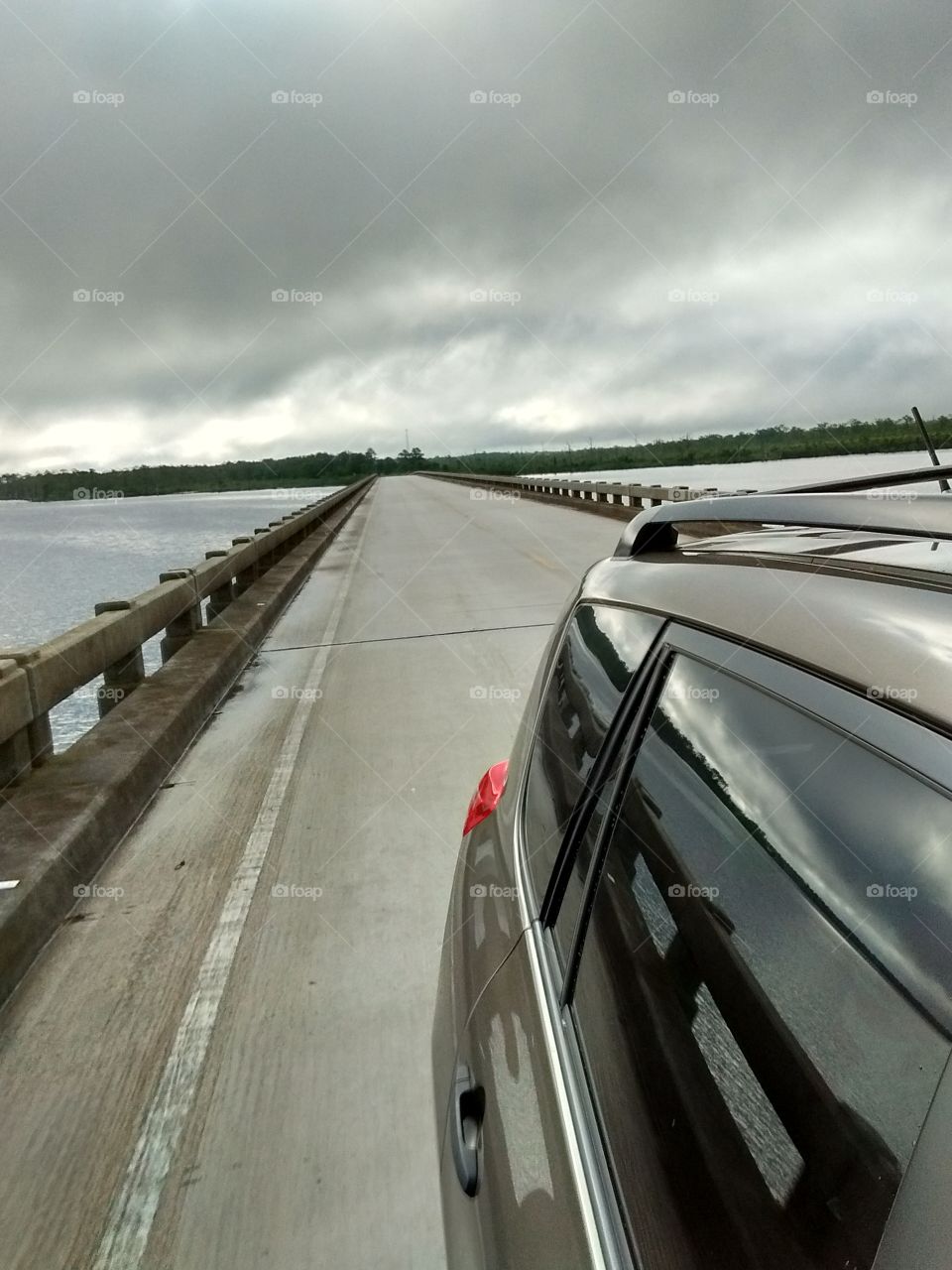 driving across a long bridge with a gray sky above