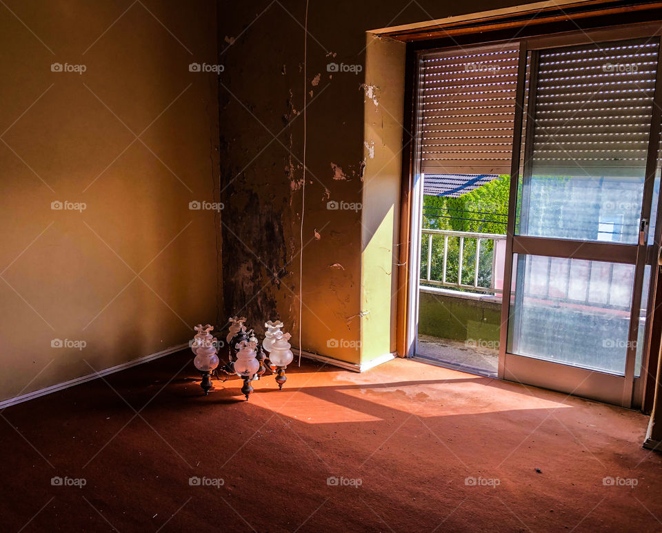 An empty room, but for a long since used candelabra stored in a dark and damaged corner. Light spills onto the old orange carpet from a half shuttered open doorway