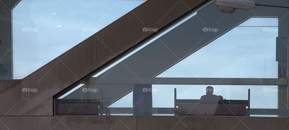 A  monochrome photo taken from street level captures the back of a person seated on a couch looking out toward the fog in New York City
