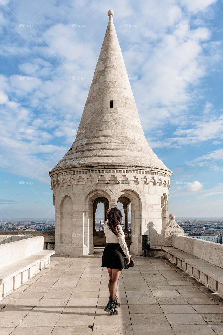Young woman standing in front of white spire at Fisherman's bastion overlooking city of Budapest in Hungary