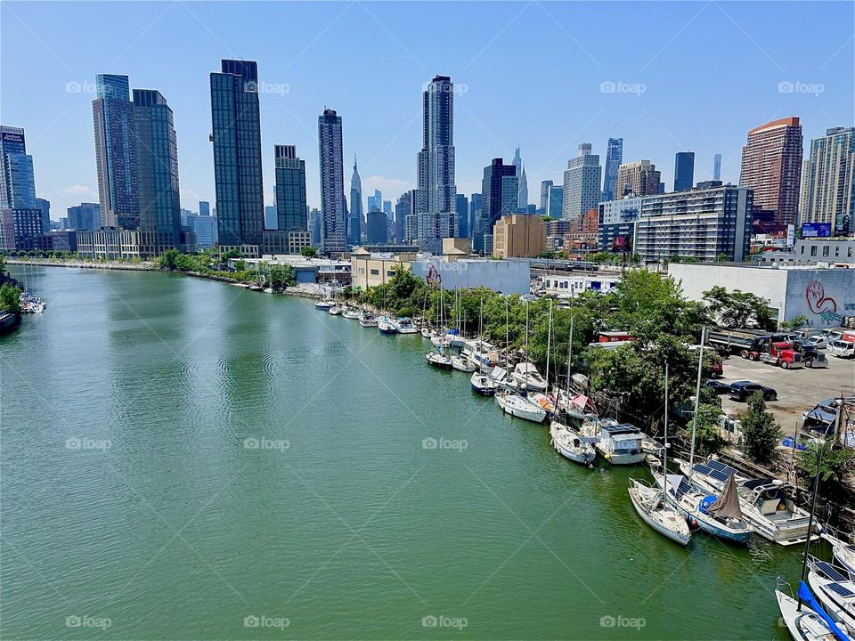 This is “Newtown Creek” with its numerous boats seen from the “Pulaski Bridge” that connects “Greenpoint”, Bklyn to LIC, Queens. Far away in the distance we see “Manhattan” and the “Empire State Building”. 2024. Hypnotic Productions