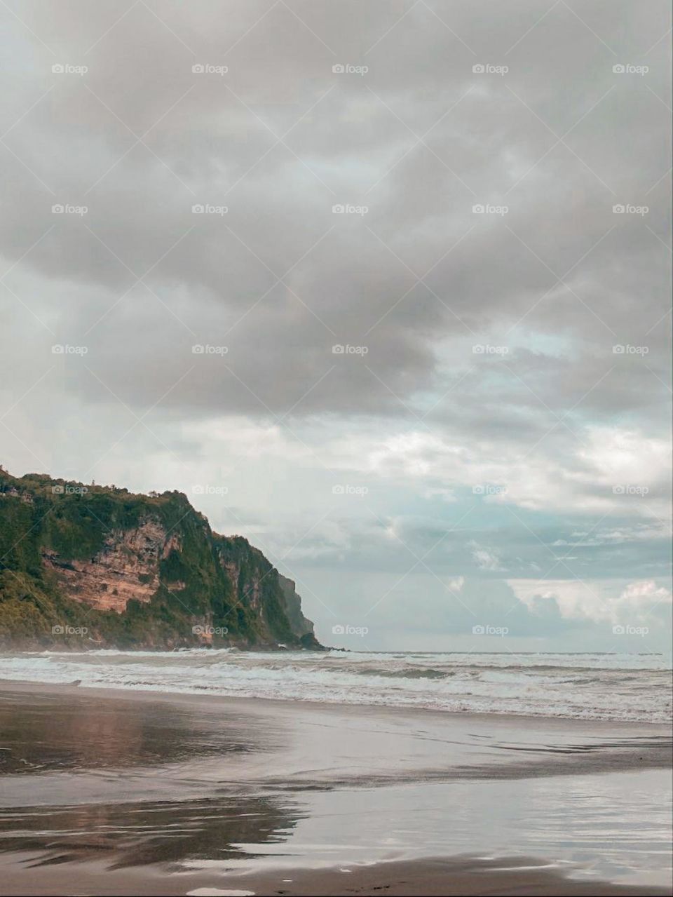 Landscape of a beach views with cloudy skies, small waves, and high cliffs in the distance