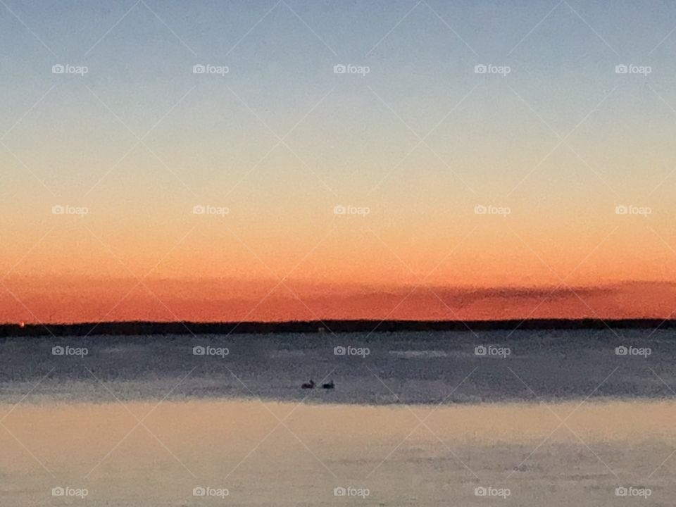 Sunset over Green Bay. Two pelicans in the center foreground. Orange and blue hues. 