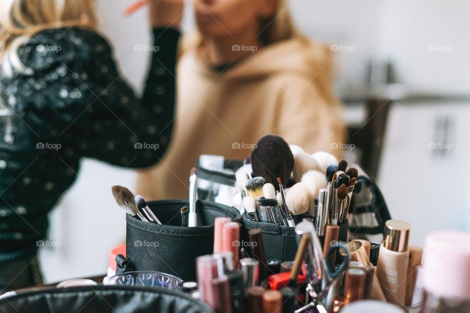 Makeup artist making makeup for woman on background of cosmetic products 