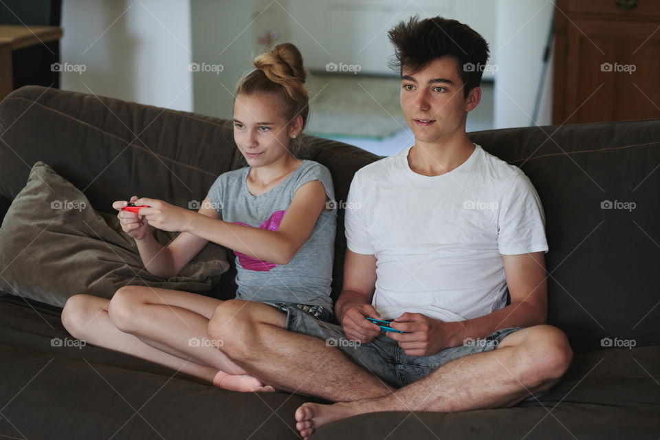 Concentrated young boy and girl playing video games sitting on sofa at home