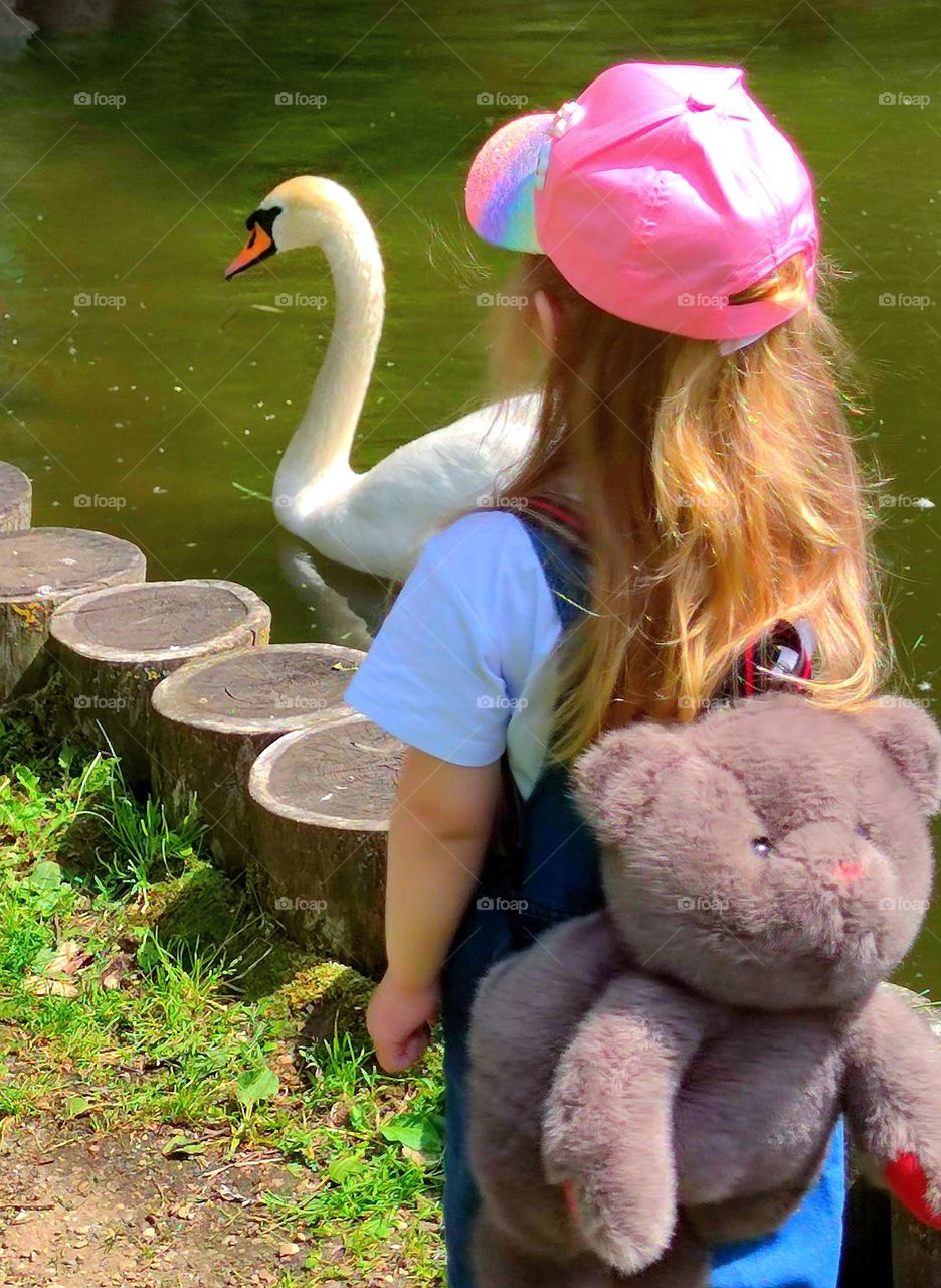 Summer Walk. Little girl with backpack and white swan in pond