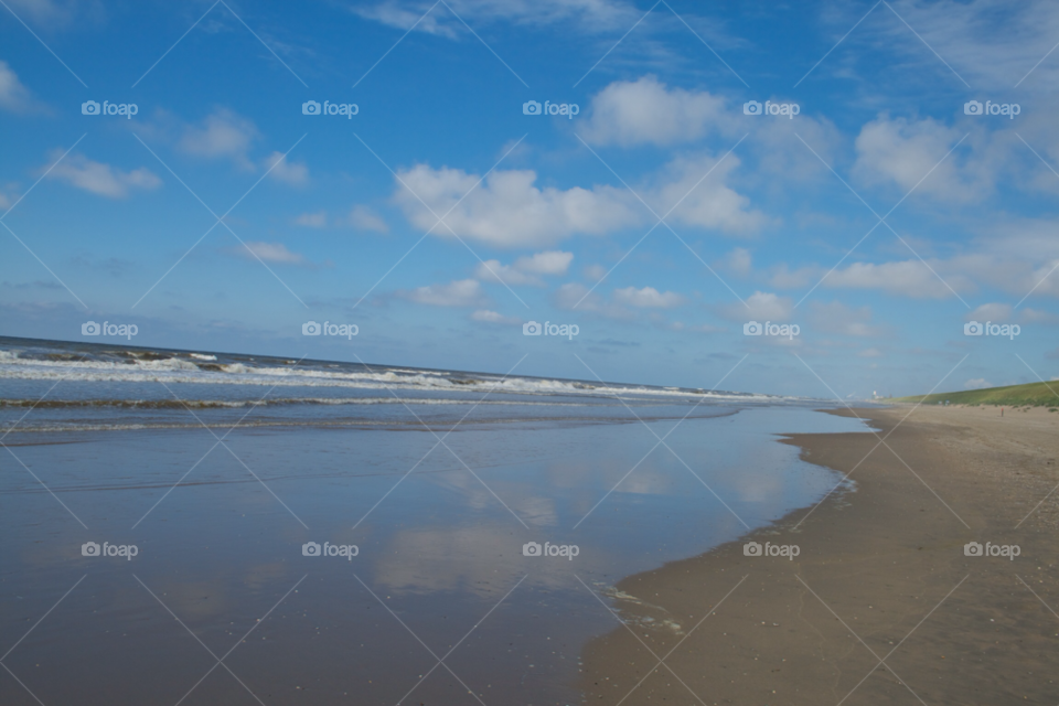 The ocean and the sky. The sky reflects in the wet sand on the beach. 