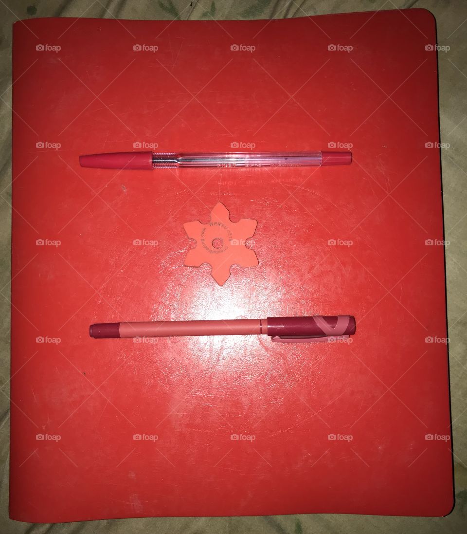 Two red pens and a red eraser on a red binder.