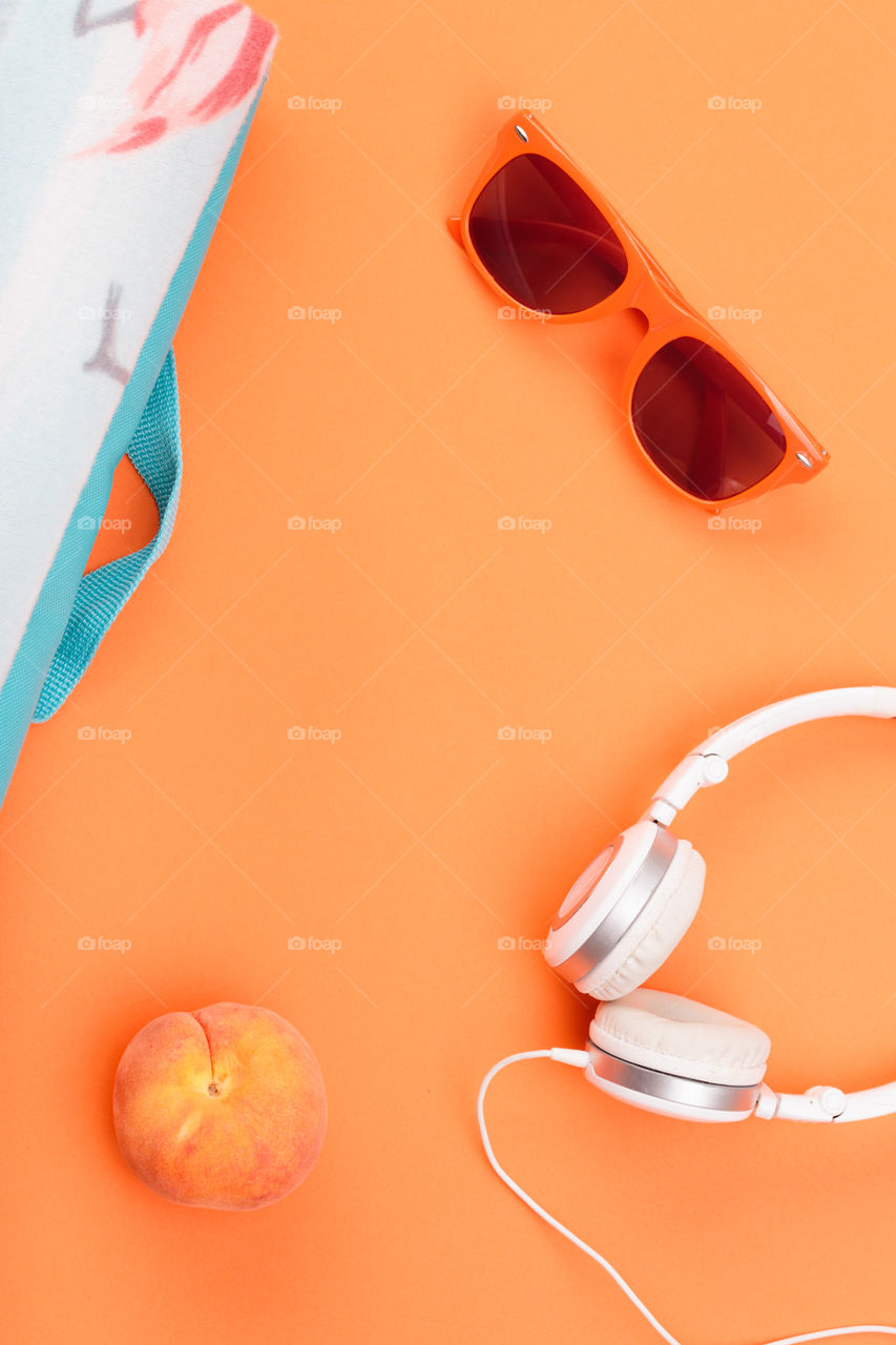 Sunglasses, glass with drink, headphones, peach, blanket on orange background. Minimal summer style