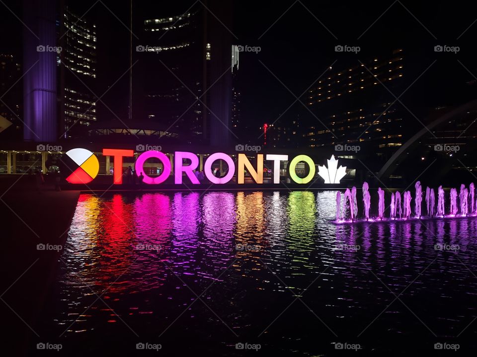 Late summer night shot of the Toronto sign, neon lights reflect of the man made pond in Nathan Philip's Square.