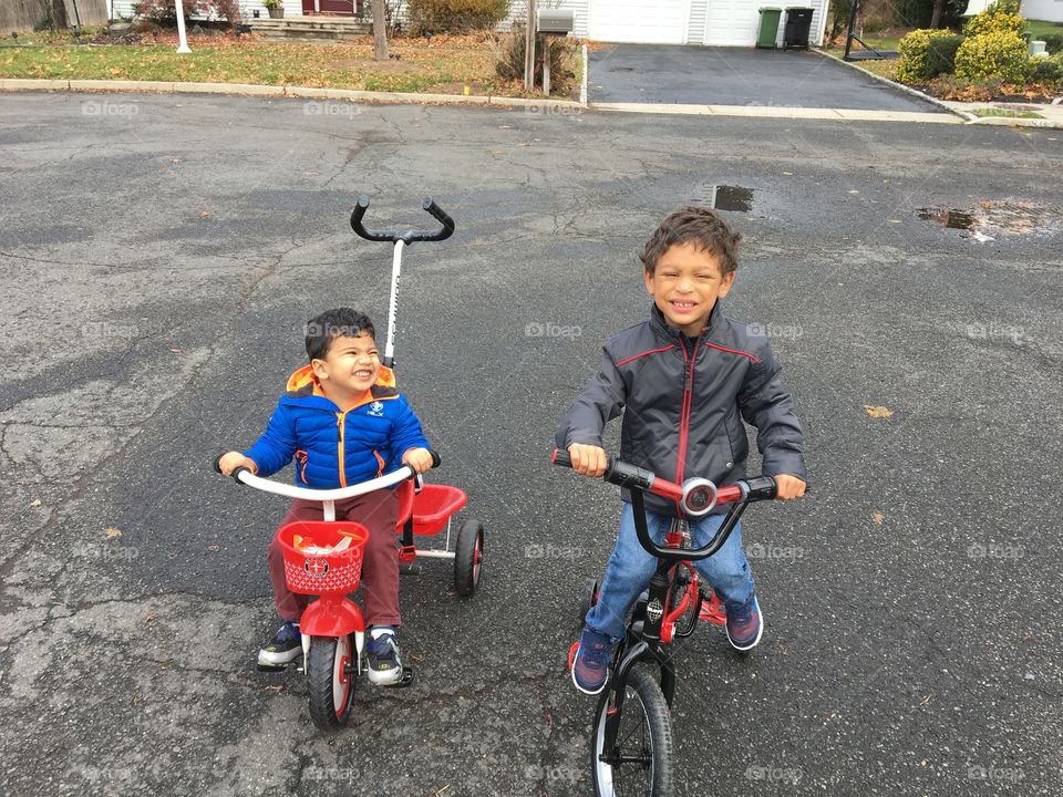 Two boys riding in the street on bicycles.