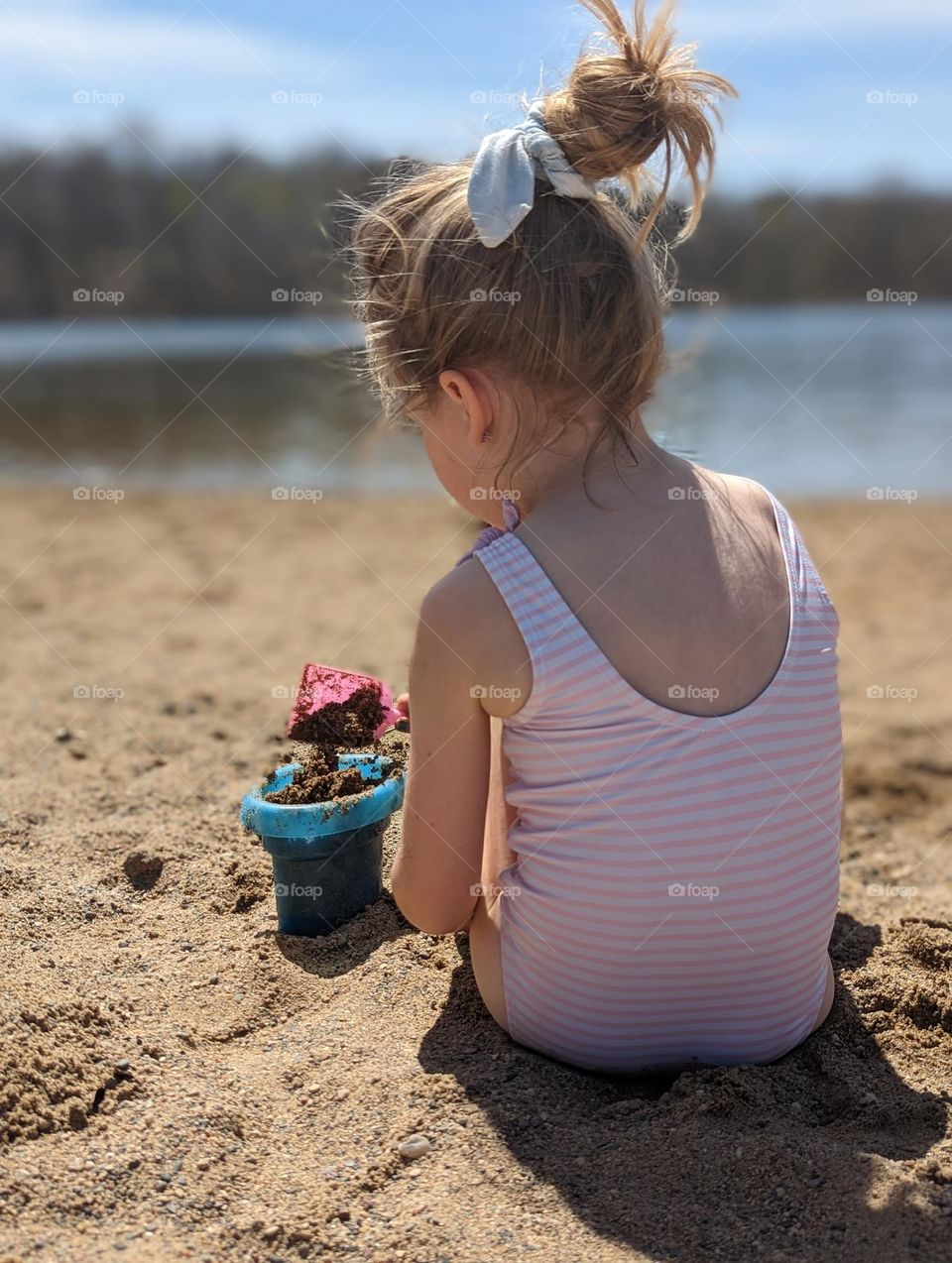 cute little girl at the beach playing in the sand and building sand castles by the lake on a sunny warm spring day