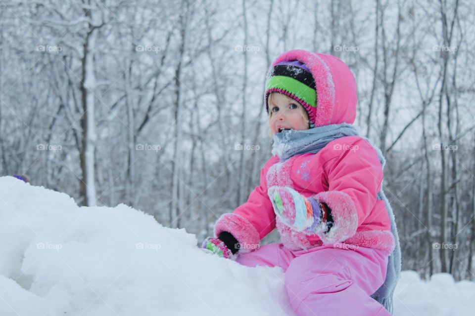 Darling little girl playing on a snow hill in her bright pink snow coat and striped hat and mittens. 