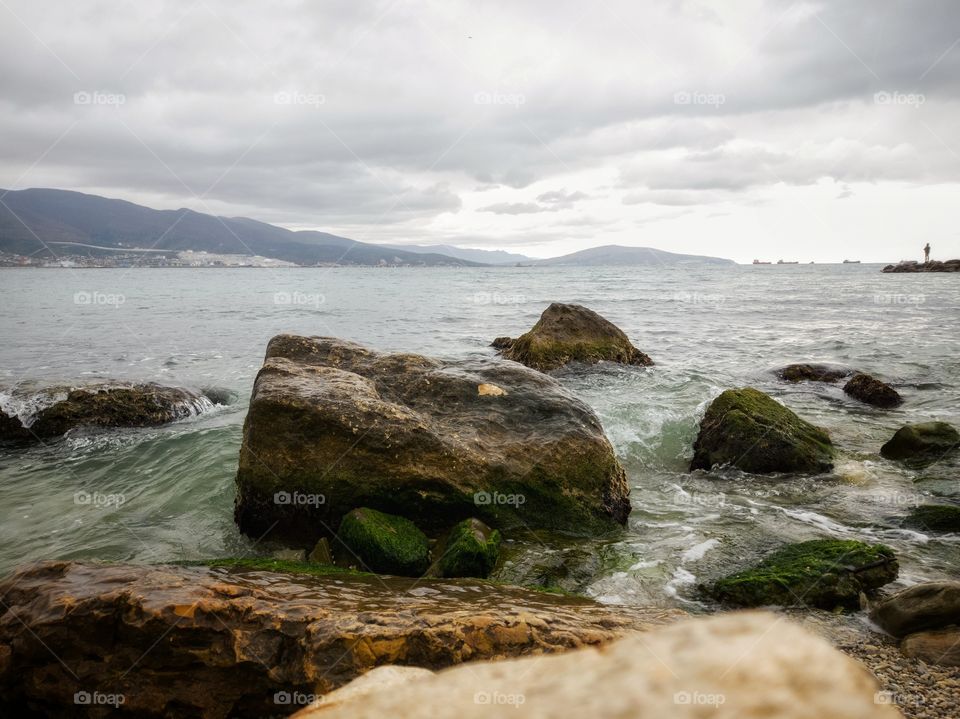 Stones overgrown with algae. It's raining. The waves of the sea. Mountain range.