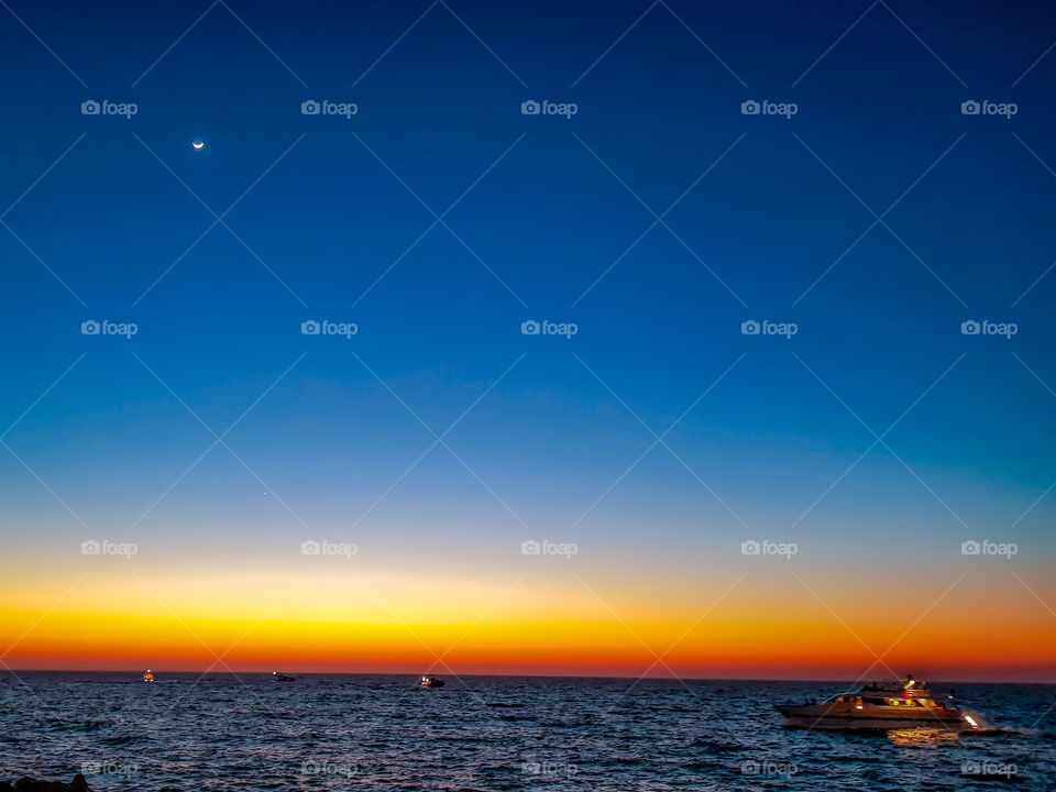 amazing sunset at the sea while the moon is out with clear blue red sky and ships passing on the calm ocean in Dubai. sun and moon in the same sky create the most beautiful scenery just compare their size