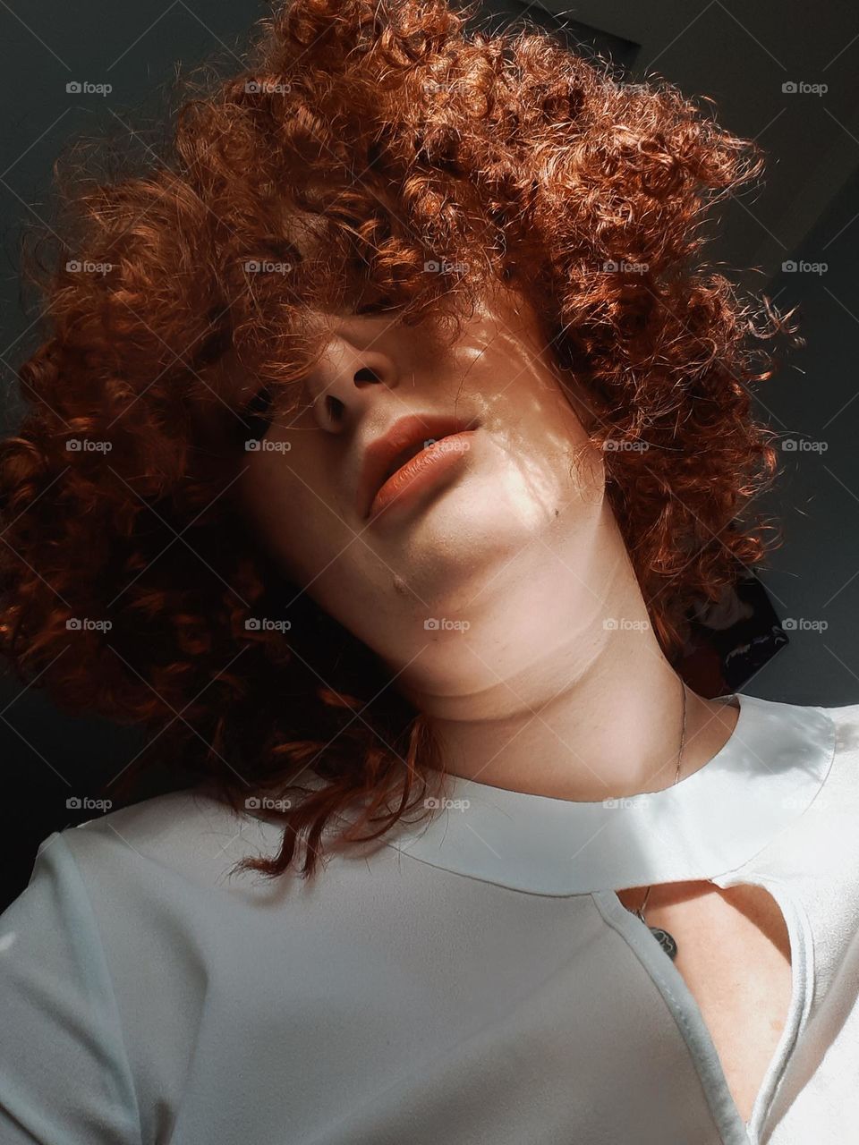 portrait of a red-haired, fair-skinned girl with curly hair covering her face, bottom view