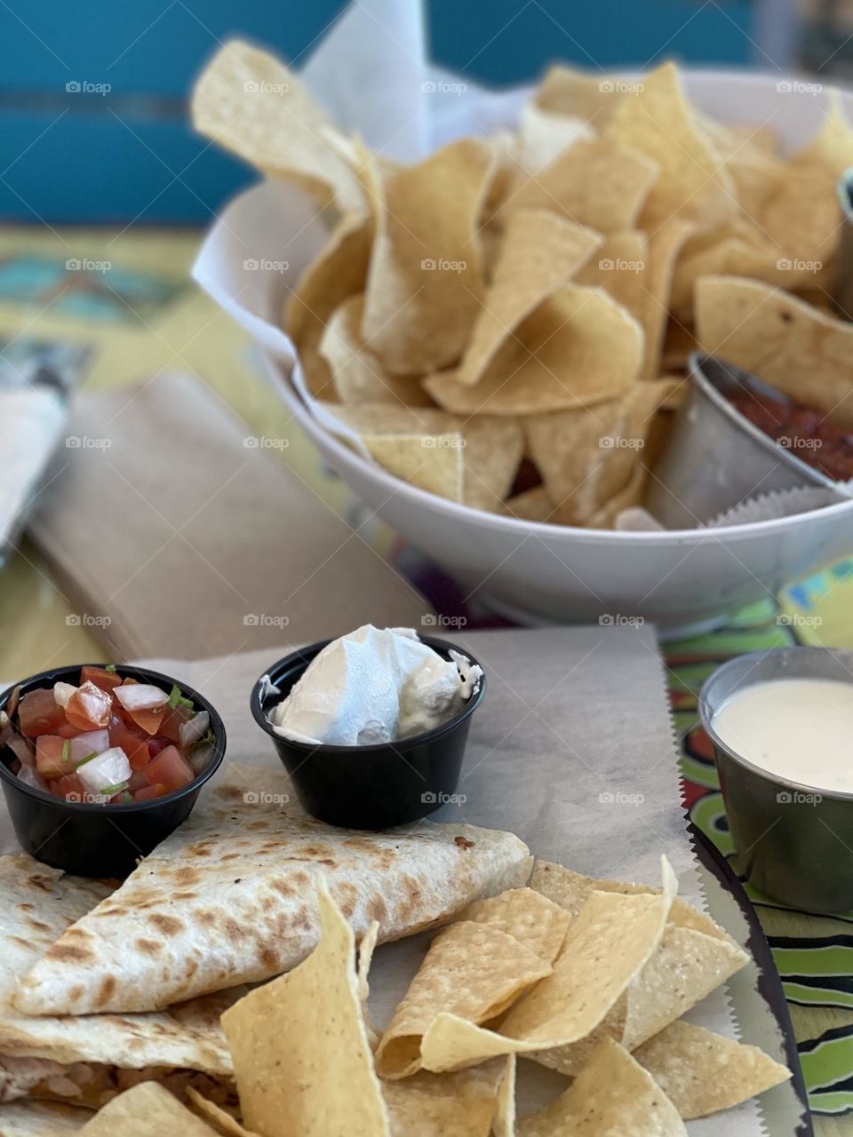 Mexican food ready to be eaten at a restaurant. The gooey quesadilla with sides is delicious. The chips and salsa looks amazing.