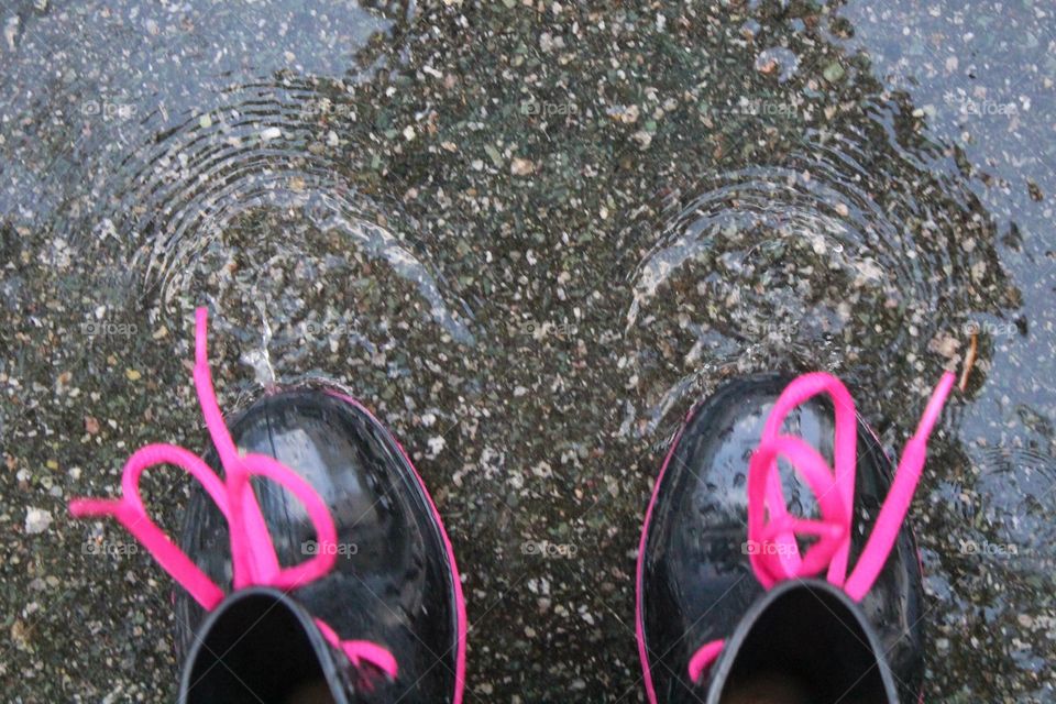 Black rain boots with pink laces jumping in puddles