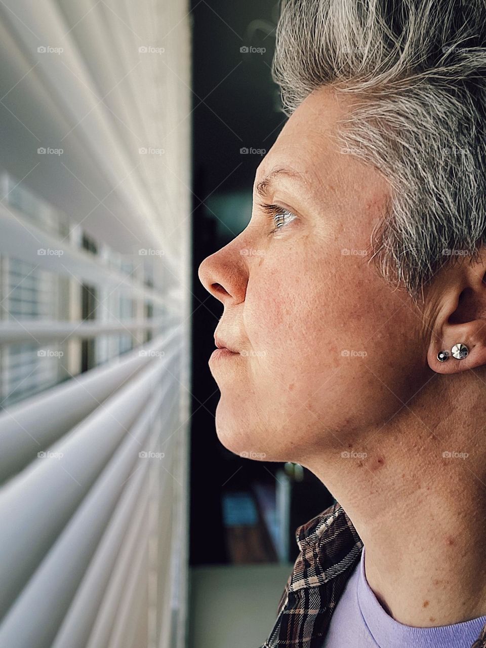 Woman looks through blind out of window, woman looks outside, woman at a window, people in windows, standing close to a window, looking out of a window, watching happenings out of the window