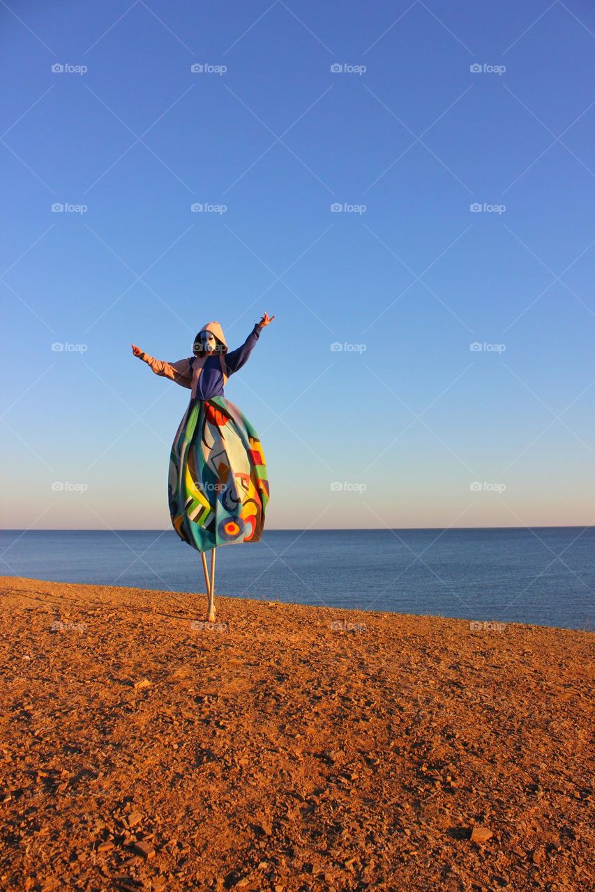 interesting outfit for a carnival; an unusual model in a mask stands on stilts on the seashore