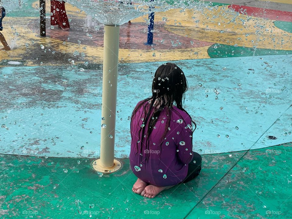 Children having lots of fun in the water at the colorful kids splash pad at the city park for children during a really warm day in Florida.