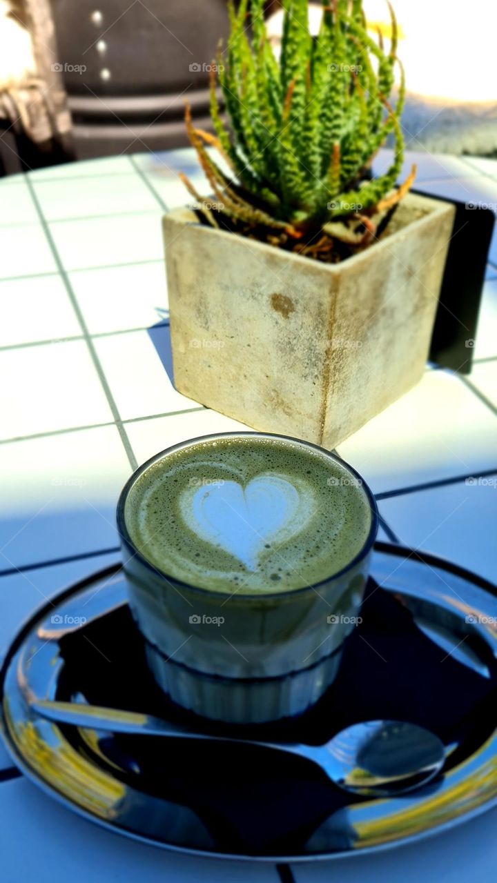 Matcha tea with heart pattern on the table, outdoor cafe, sunny day