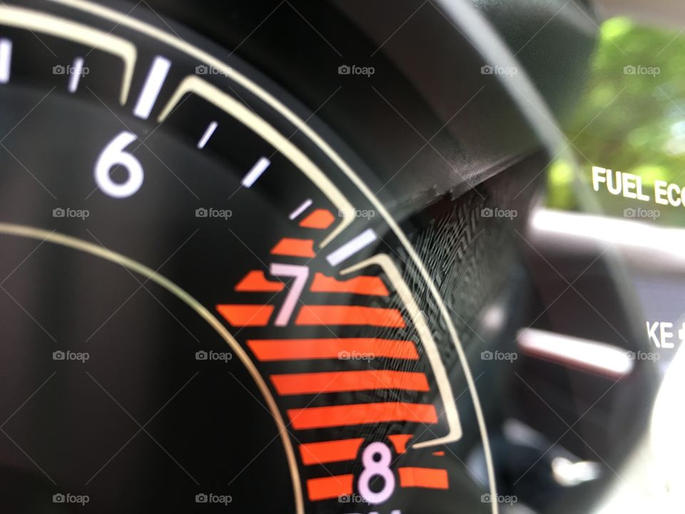 Speed gauge and orange rpm and fuel economy conceptual driving and environmental car shopping photography closeup full frame with reflection of trees 