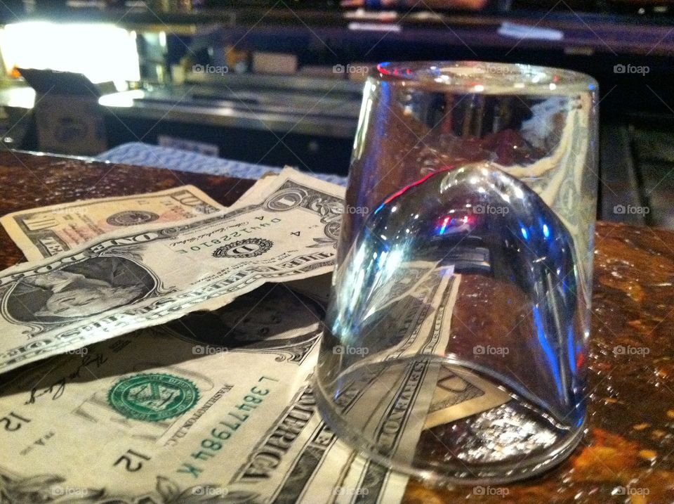 Cash and a shot glass sitting on a bar.