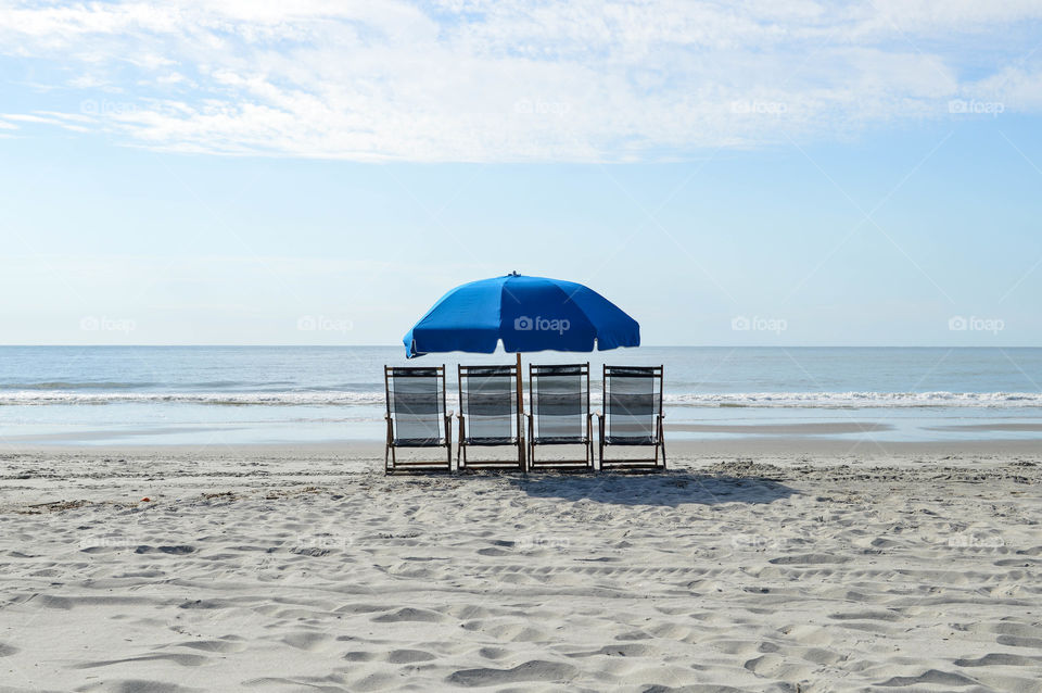 Row of empty lounge chairs with an umbrella on the shore of the beach