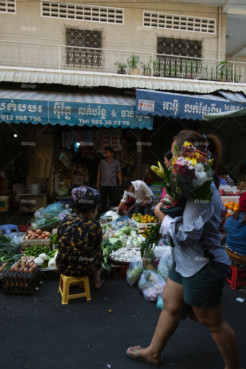 Women in the market selling vegetables and carrying flowers