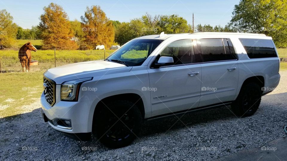 GMC Denali SUV parked on a rock drive in front of the horse pasture in fall