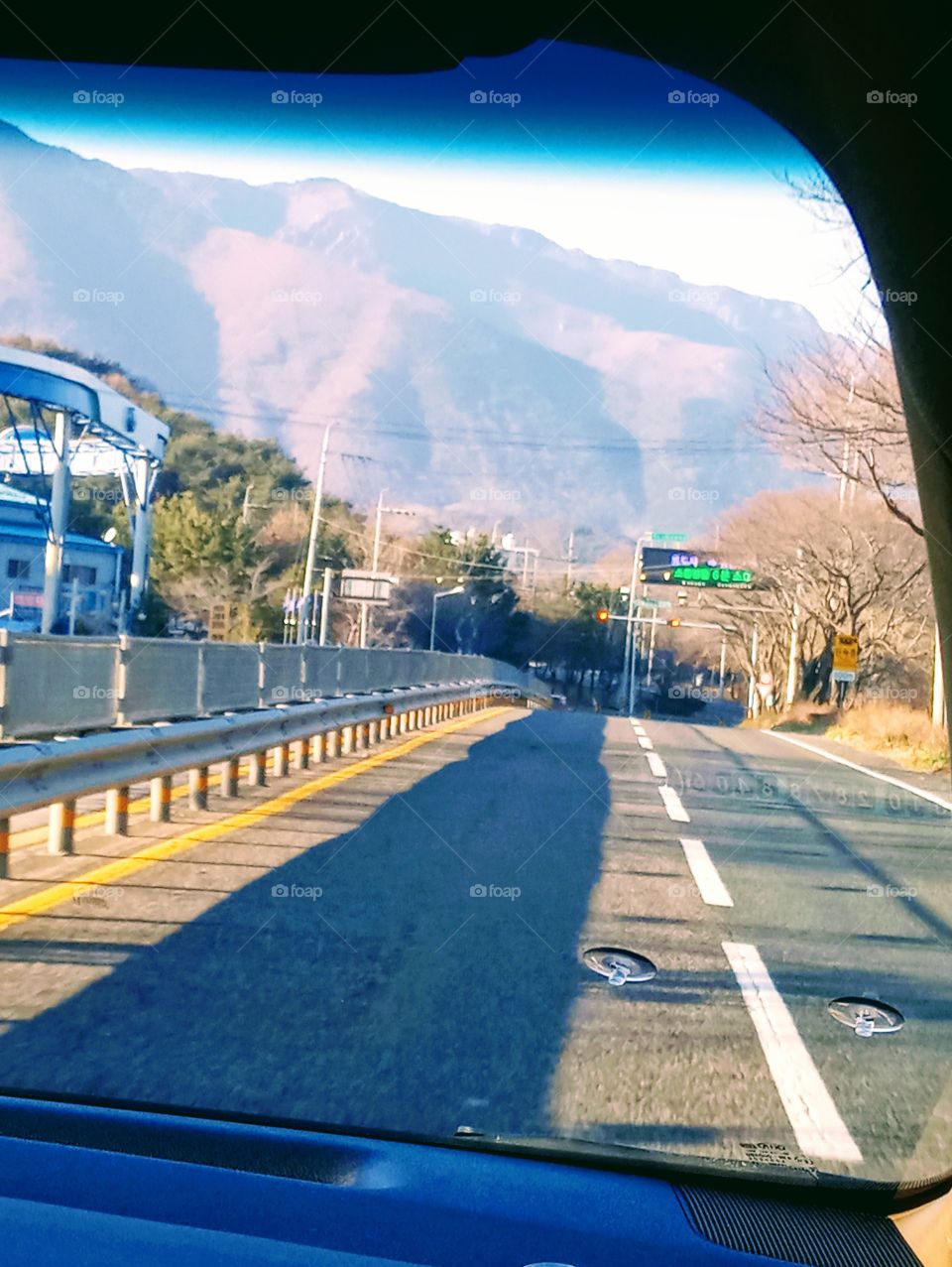 The Road to our way Home where you can see alot of trees beside the road and the gasoline station at the left side.
In far front you can see the very high mountains.
thanks to the sunlight the places becomes more lively.