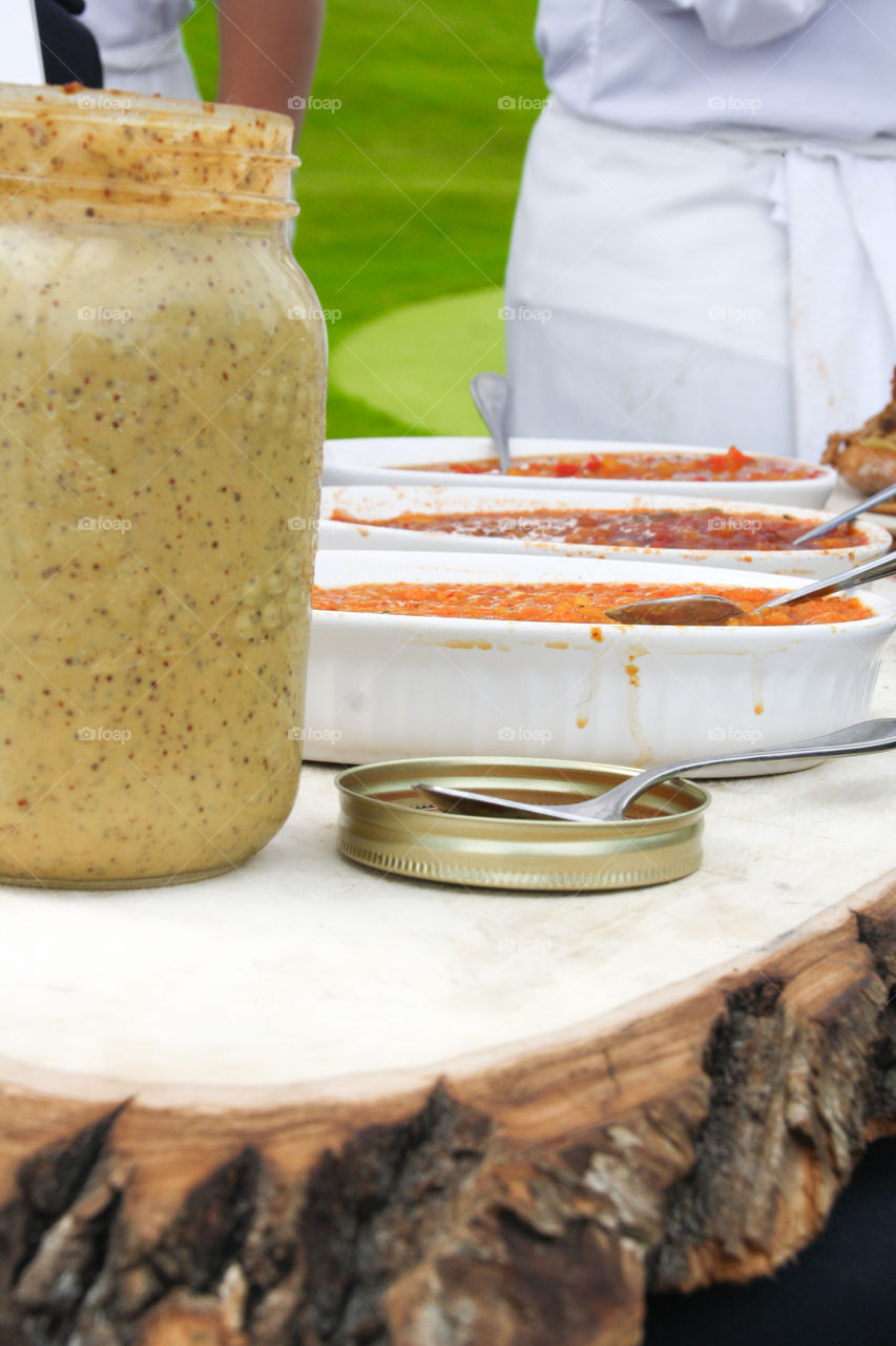 A beautiful buffet meal is laid out in a rustic block of wood, ready to be served with condiments with a mason jar in the foreground