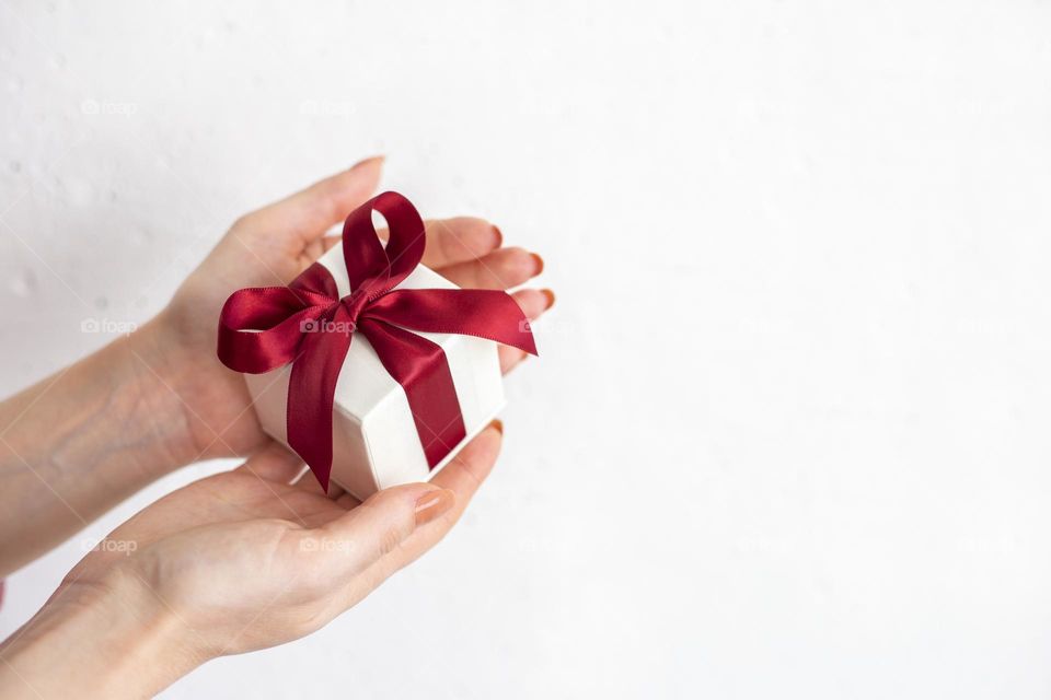 Female hands holding white gift box with red bow on the white background 