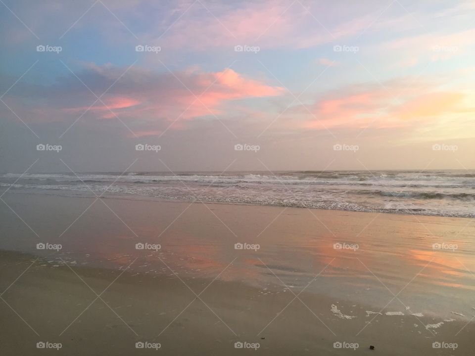 Sunrise with pink clouds and blue sky reflecting on the water at the beach with waves in the background 