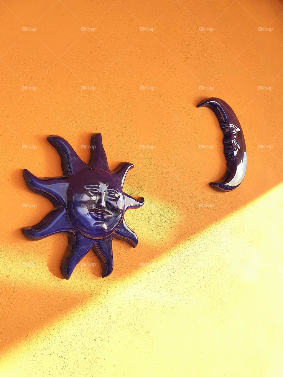 ceramic blue sun and blue moon, hanging on the house wall, with a play of shadows from the sunlight