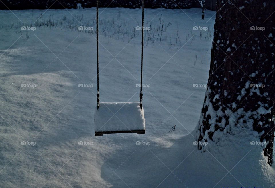 Close up on an oak tree swing and ground underneath covered with fresh snow in a private garden in Maintenon