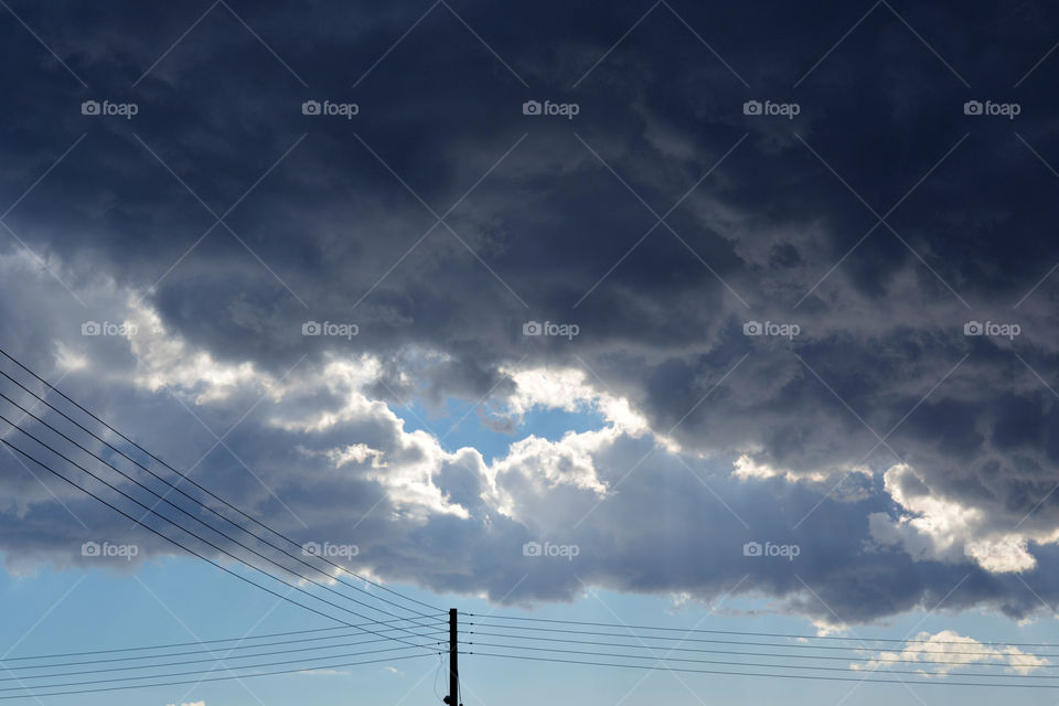 Blue sky with white and dark clouds above the electric pole.
