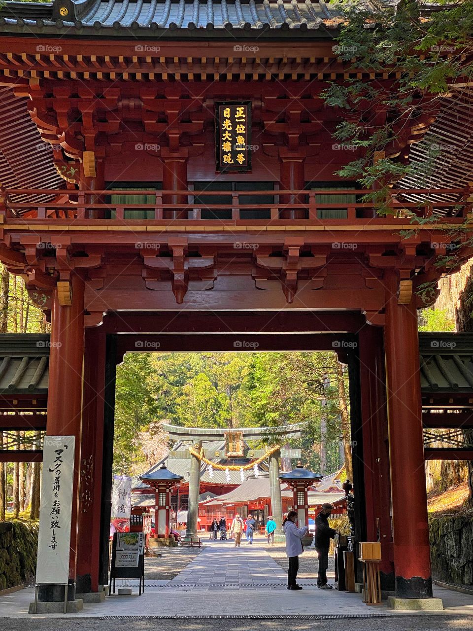 Beautiful huge towering red wooden gates at Nikko Futarasan Shrine, with torii gate and rope decor on the other side.