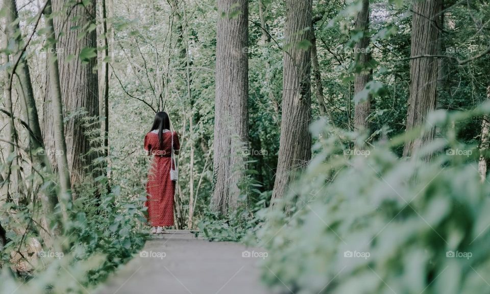 One young caucasian brunette girl with long flowing hair from the back walks along a wooden winding path in the forest on a summer day, close-up side view.