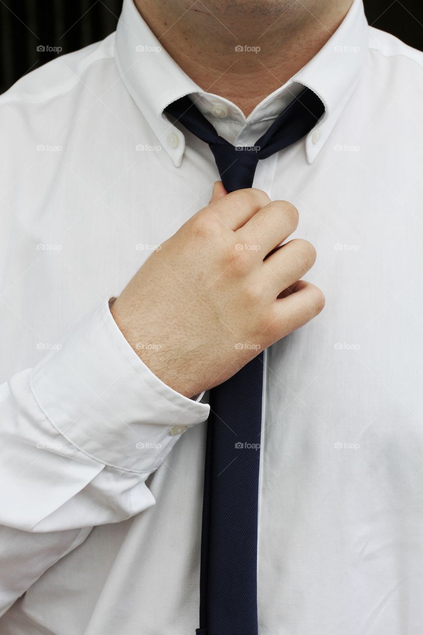 A man in a shirt and tie and unbuttoned collar doing up his tie.