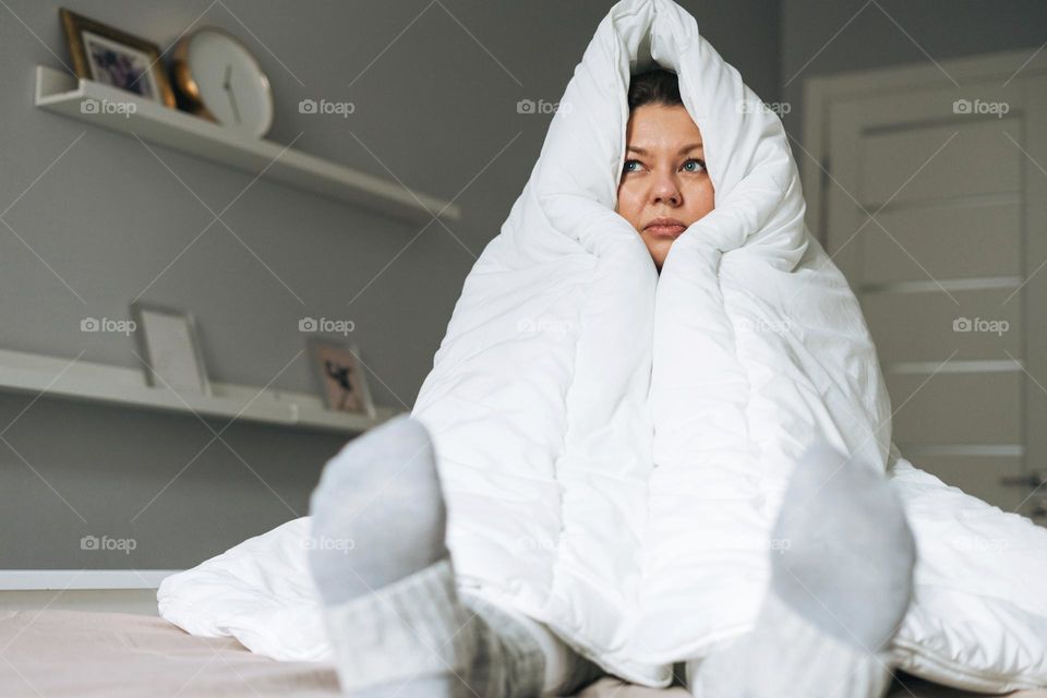 Young adult unhappy lonely woman forty years plus size body positive in white big blanket on bed at the home