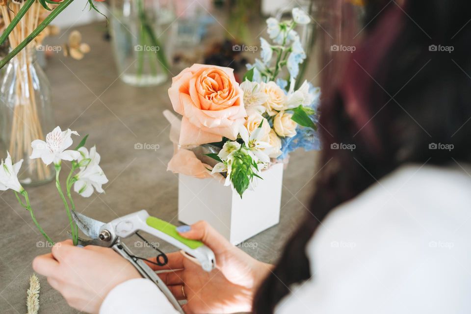 Young woman florist in white with bouquet of flowers in box in flower shop, small local business owner. Young stylish success millennial woman on the creative work