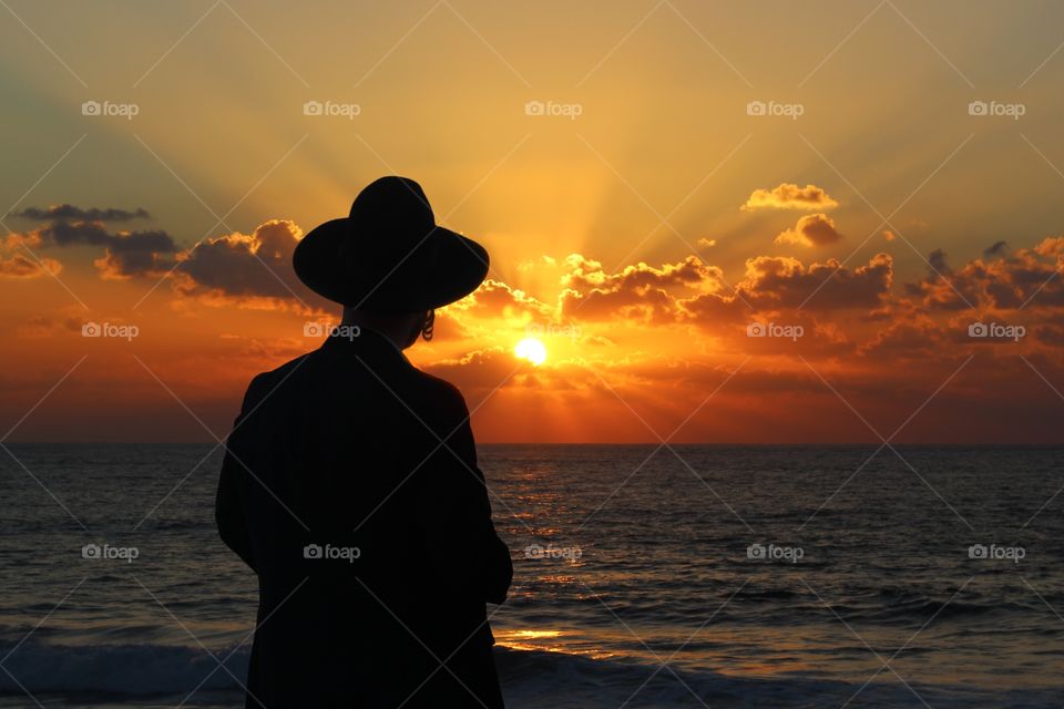 A religious Jew standing on the coast of Mediterranean sea and watching the sunset, deep in thought.