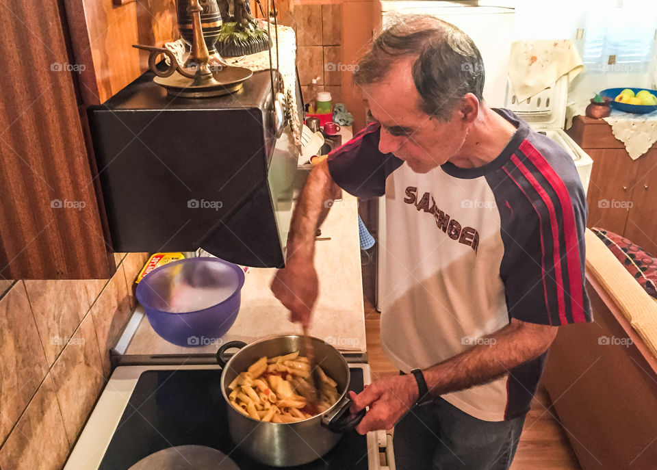 Man In The Kitchen Cooking Penne Pasta Macaroni With Tomato Sauce In A Pot
