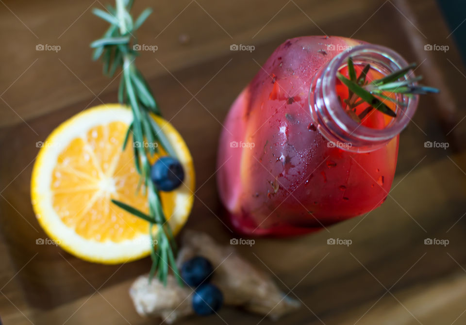 Beautiful summertime drink with fresh ginger, orange, blueberry juice, and garnished with rosemary elevated view on dark wood gourmet food photography 