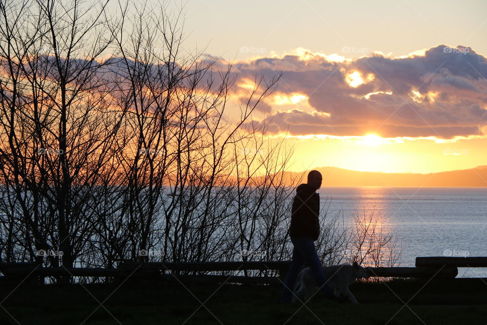 Man walking by the shore watching sun casting its light into the ocean 